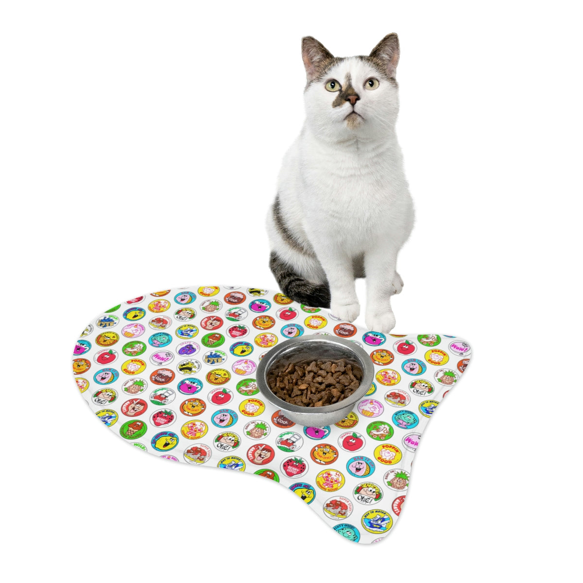 Cat beside fish-shaped feeding mat holding a food bowl, multicolor print.