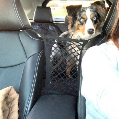 Australian Shepherd sitting behind a mesh car barrier net between the seats, preventing front-seat distractions.